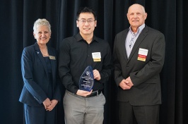 A man holding an award stands between a woman on the left and a man on the right