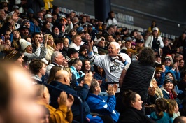 An older man waves his hat to the crowd at a hockey game