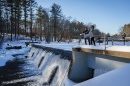 Two researchers, one man and one woman, stand on a snowy bridge over a small waterfall